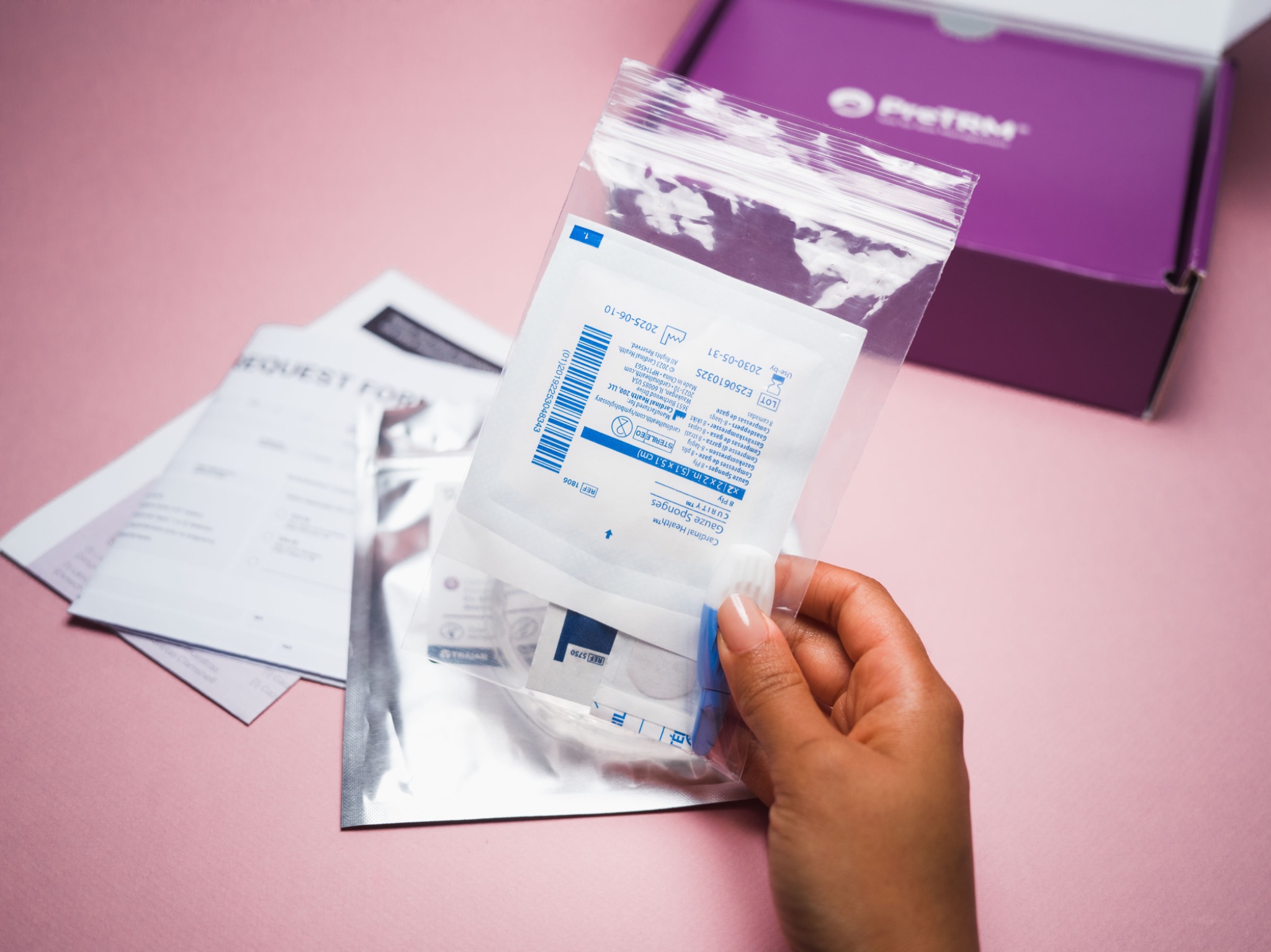 Hand presenting a PreTRM sample bag beside the open kit