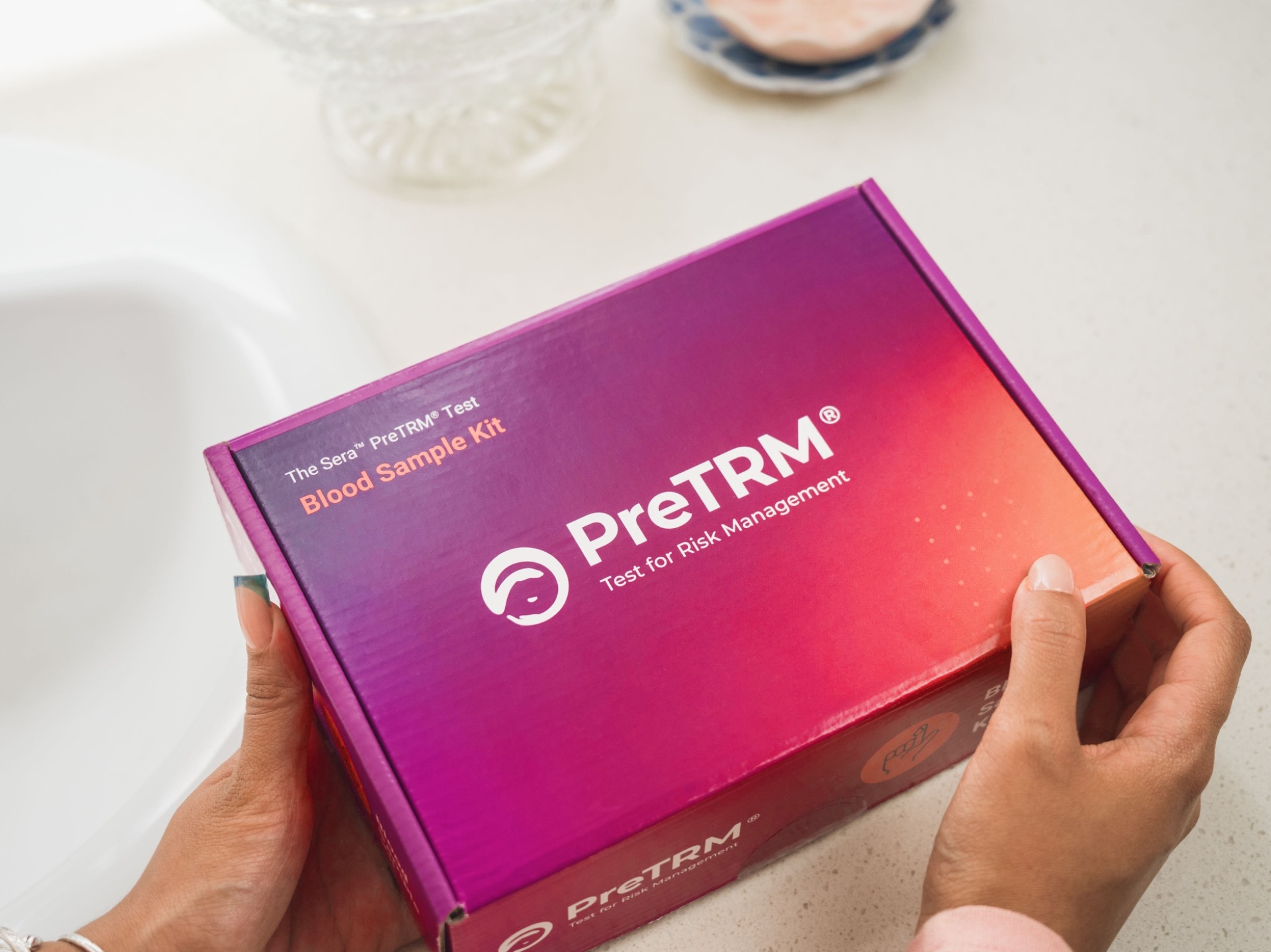 Hands holding a PreTRM kit in a home bathroom environment