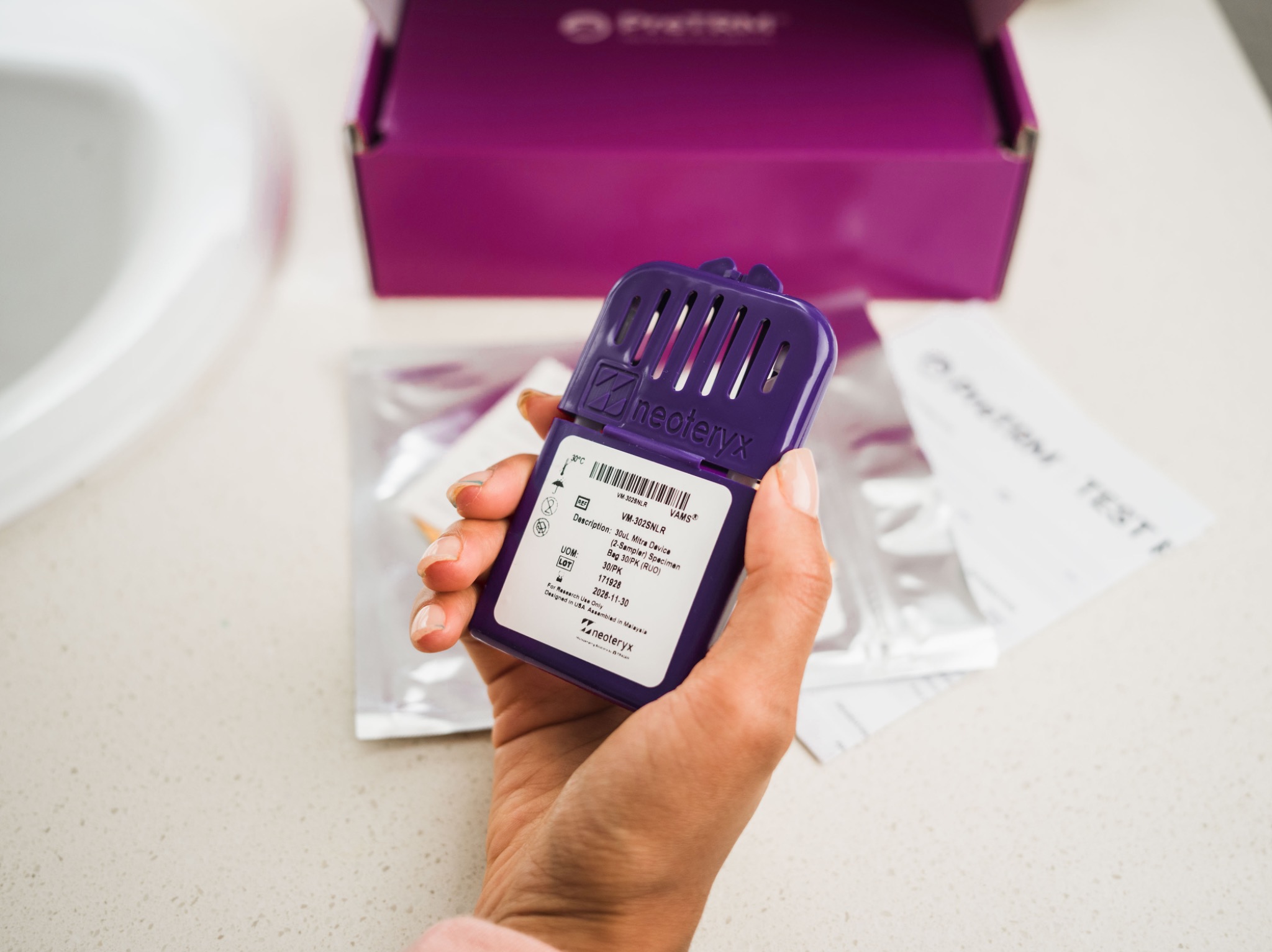 Hand holding the purple PreTRM sample device beside the open kit