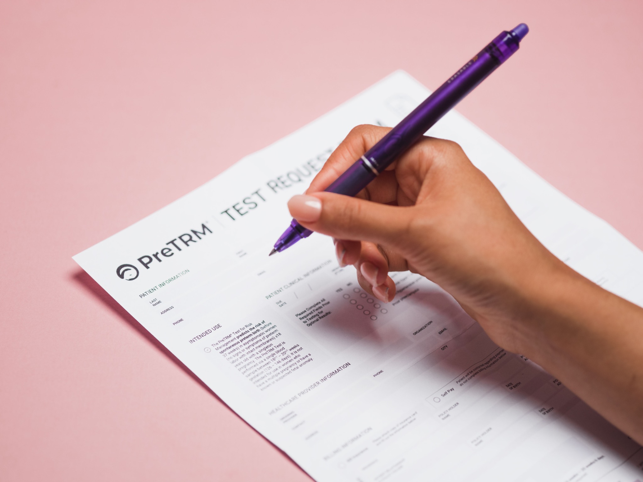 Hand completing the PreTRM test request form with a purple pen