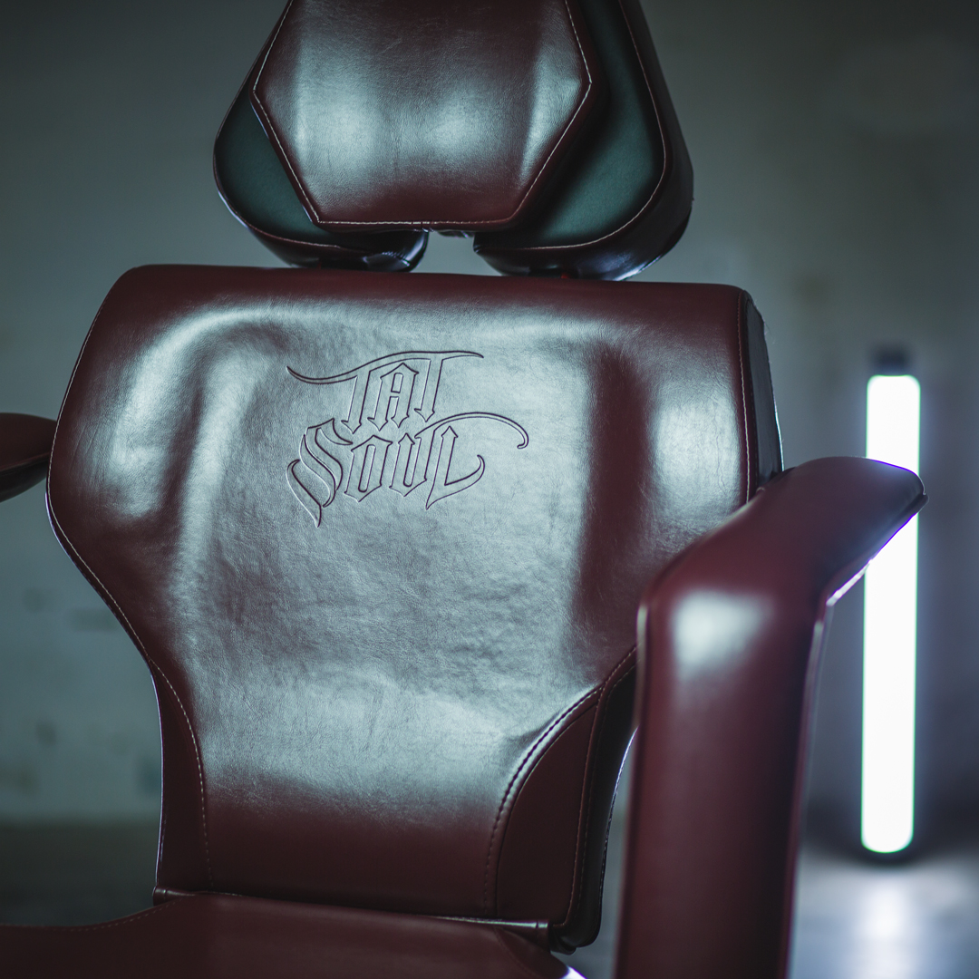 Oxblood TATSoul tattoo chair logo detail photographed with cyan and magenta practical lighting