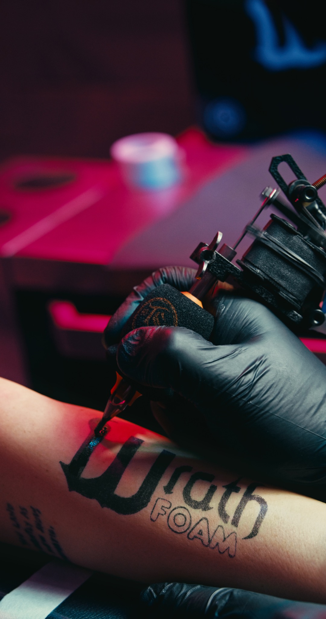 Close detail of a tattoo artist working under red and blue light